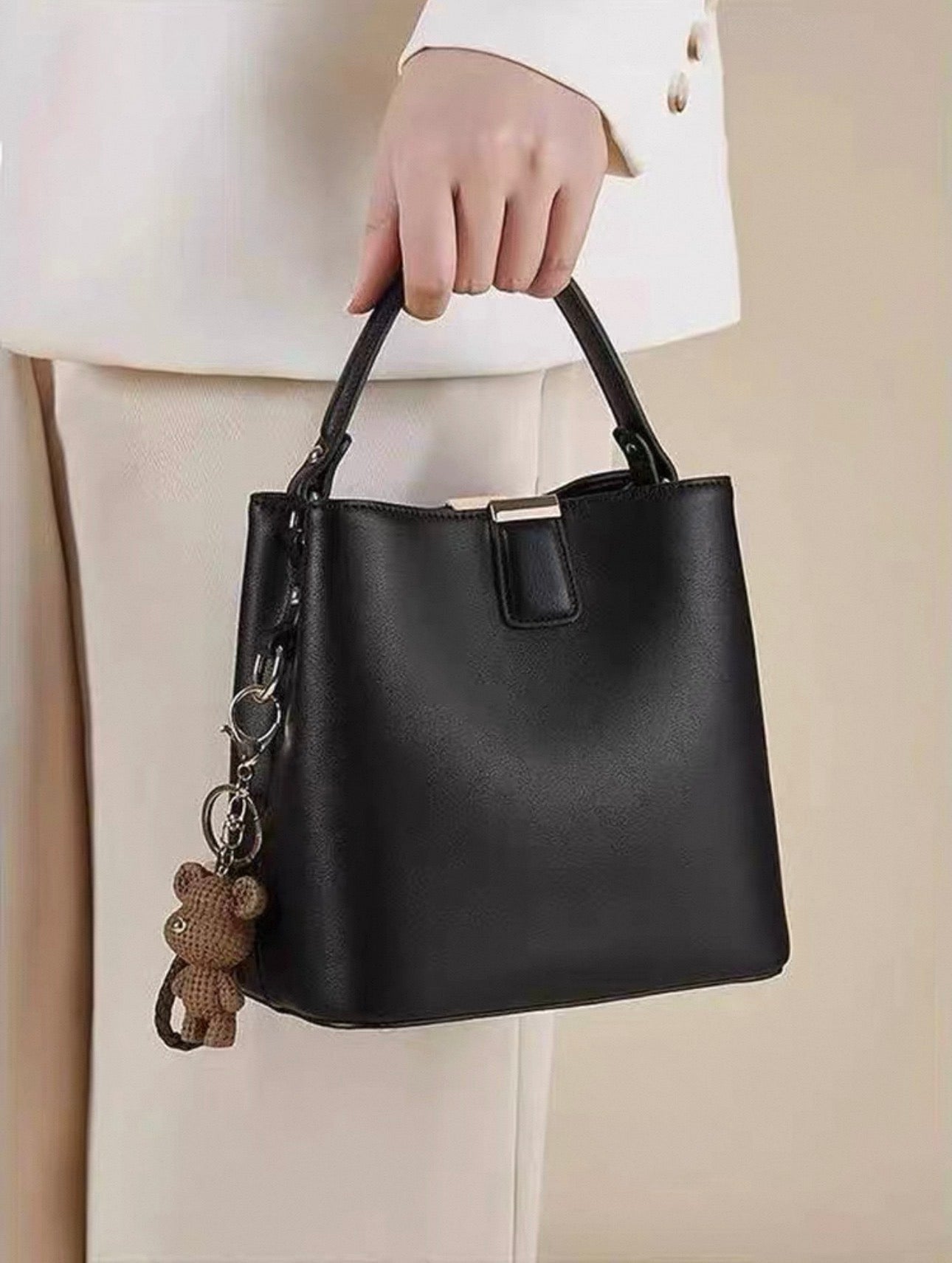 Black bucket handbag with single top handle and teddy bear charm accessory.