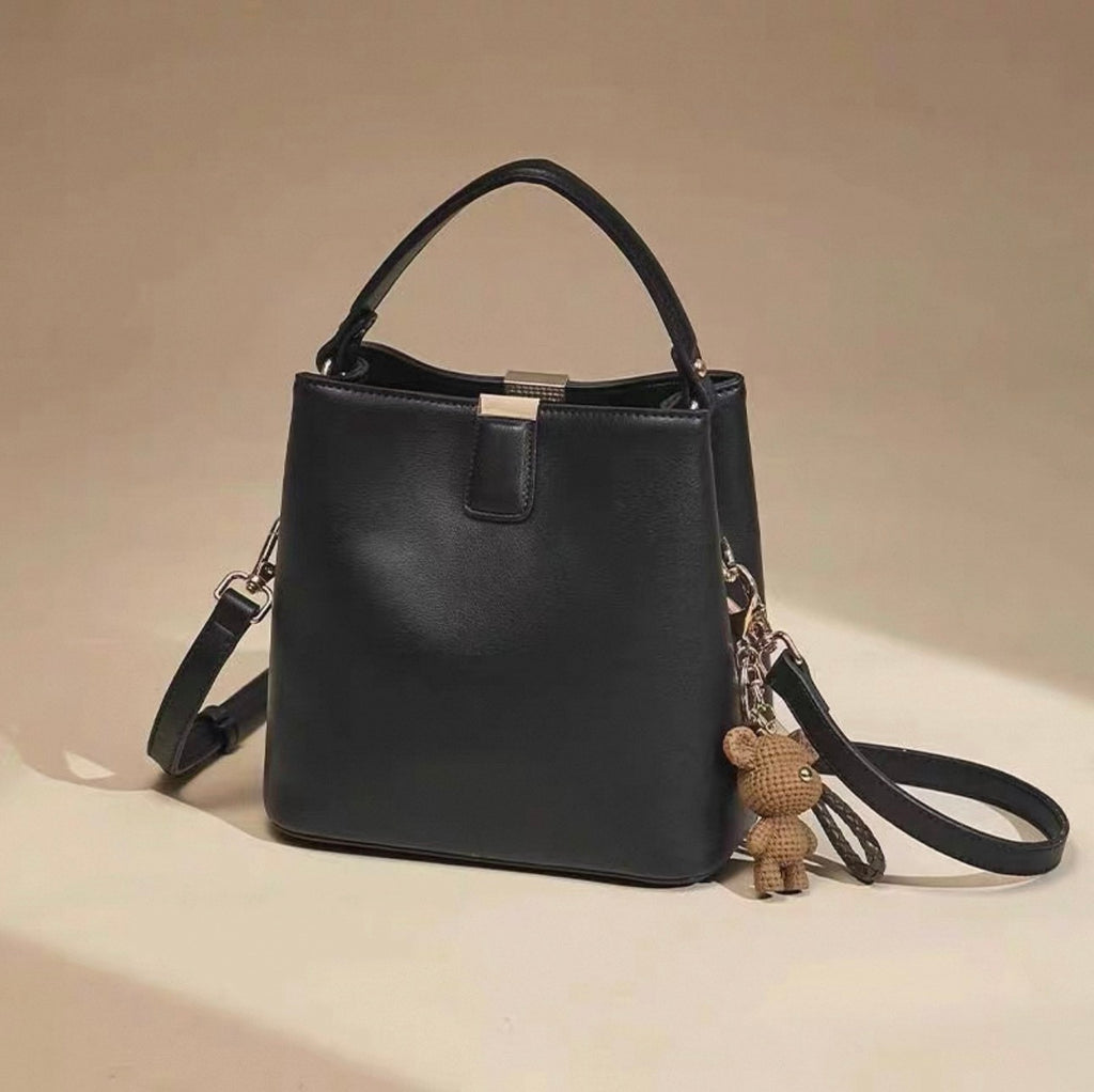 Black bucket bag with single shoulder strap, gold hardware, and small teddy bear charm.