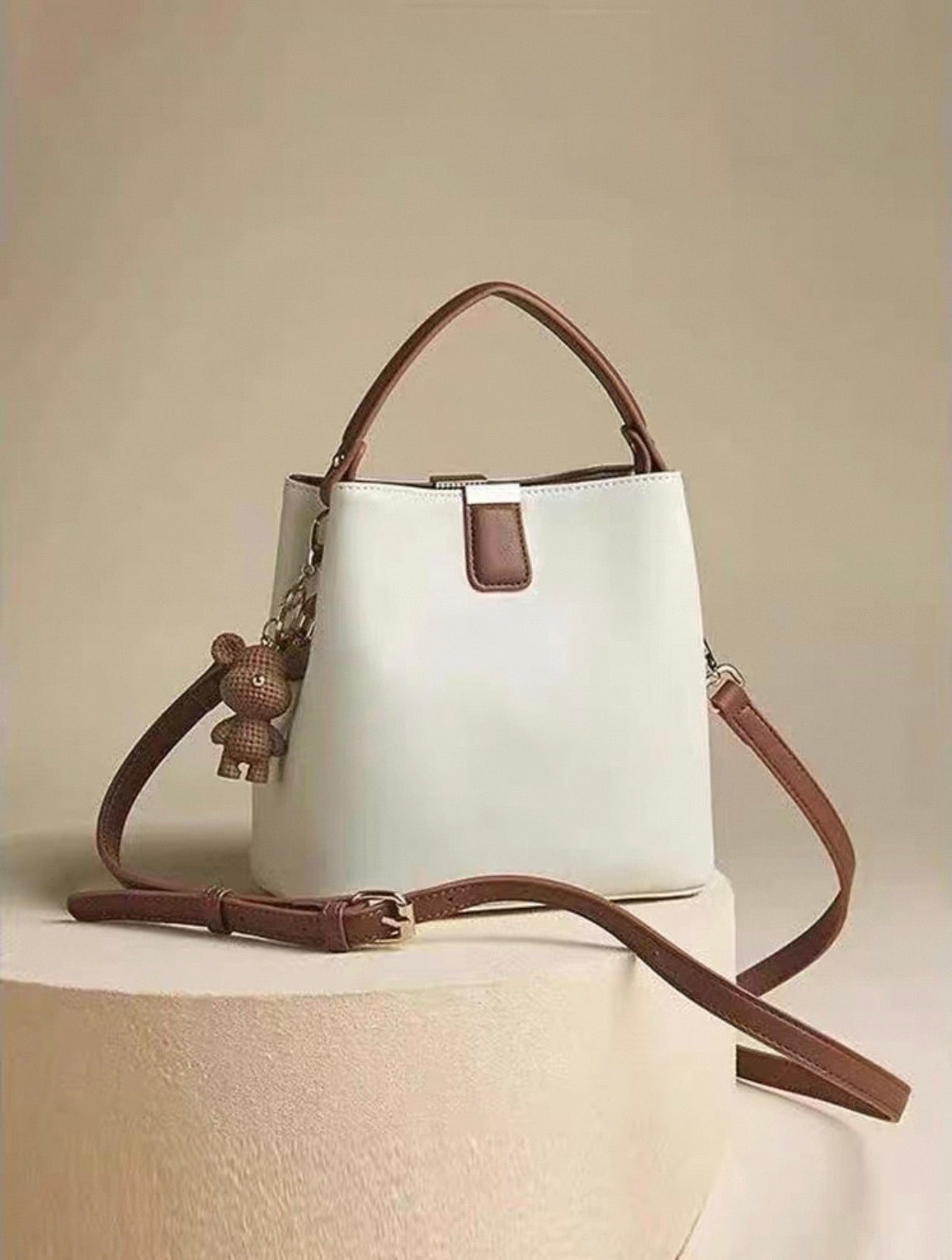 Beige and brown bucket bag with single shoulder strap and bear charm accessory.