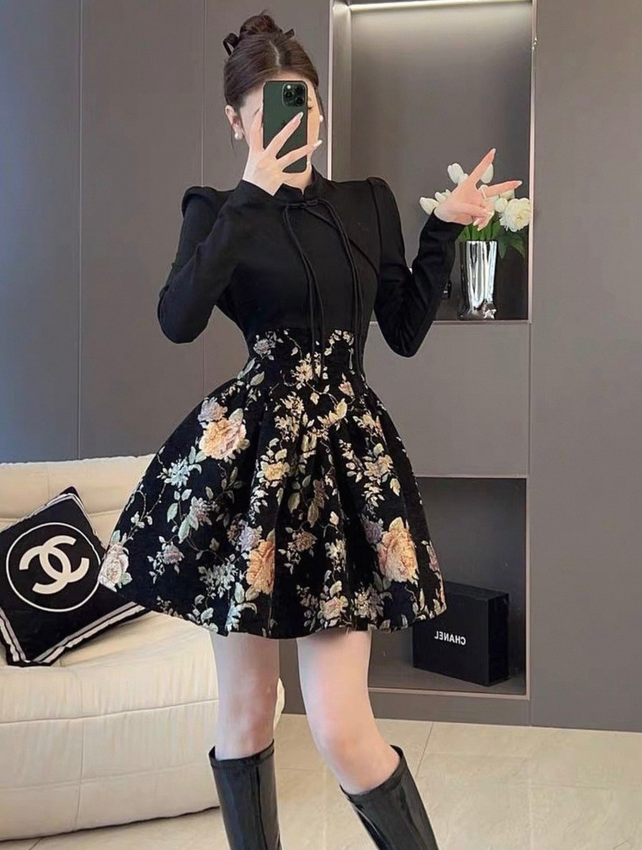 Person wearing a black outfit with a floral skirt in a room.
