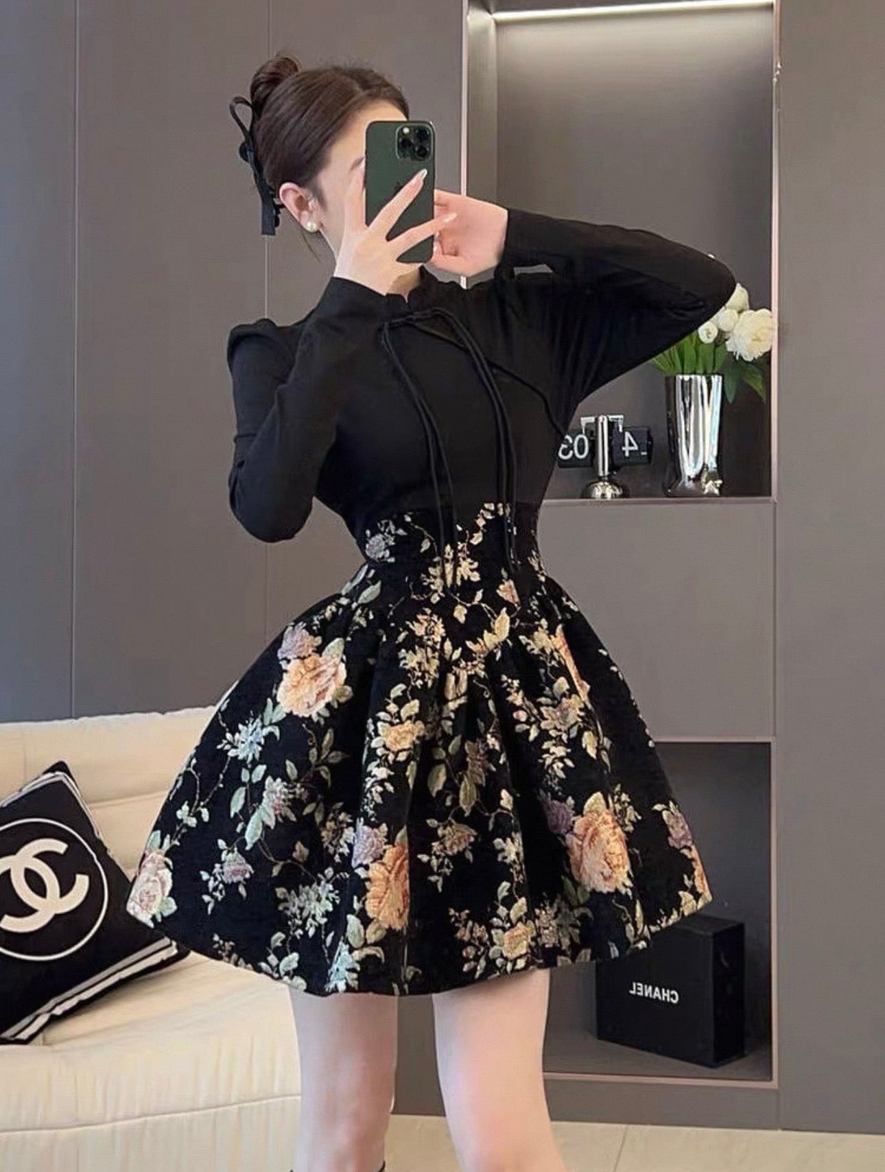 Woman taking a mirror selfie wearing a black long-sleeve top and floral skirt in a room.
