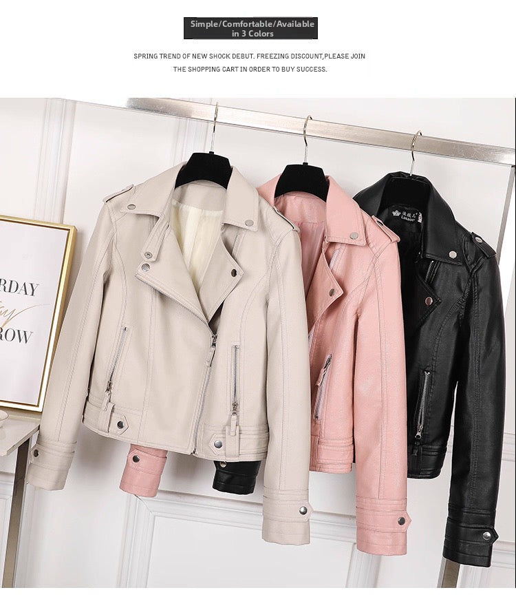 Three leather jackets in beige, pink, and black hanging on a rack against a white wall.