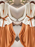 Two white tops with brown belts and pants on hangers against a neutral background.