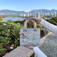 Handbag held by a person with a scenic city and mountain view in the background