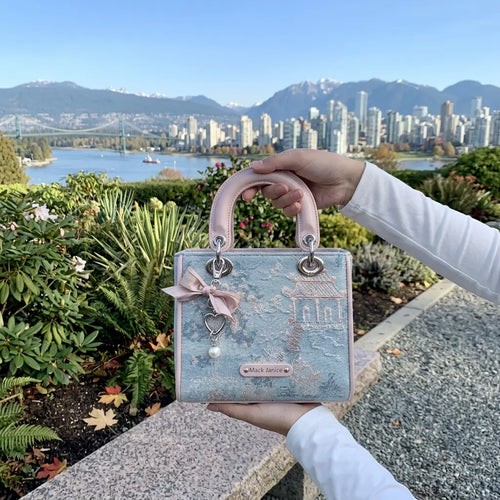Handbag held by a person with a scenic city and mountain view in the background