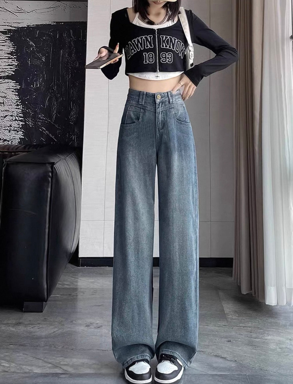 Person wearing a black crop top with text and high-waisted blue jeans indoors.