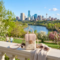 Pink handbag with sunglasses on a ledge overlooking a city skyline with a river and greenery.